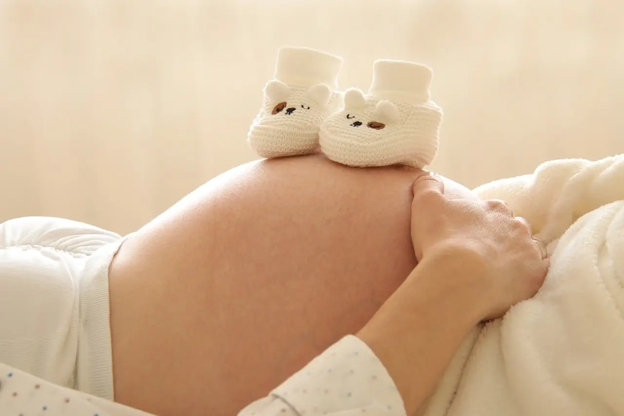 Femme enceinte avec chaussons de bébé sur le ventre Femme enceinte portant délicatement des chaussons de bébé sur son ventre pour symboliser l’arrivée de son enfant